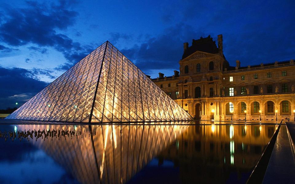 Una foto di notte del celebre museo a forma di piramide e della piazza entrambi illuminati da tante lampadine